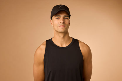 Man wearing a black tank top and cap on a beige background, showing the front of the red light cap
