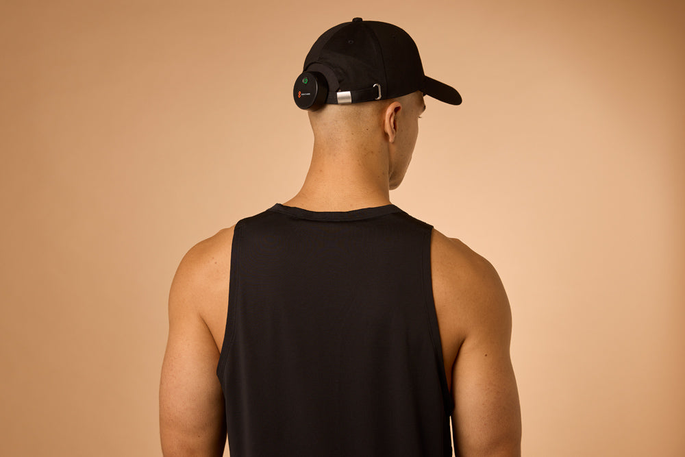 Man wearing a black tank top and cap on a beige background, showing the back of the red light cap